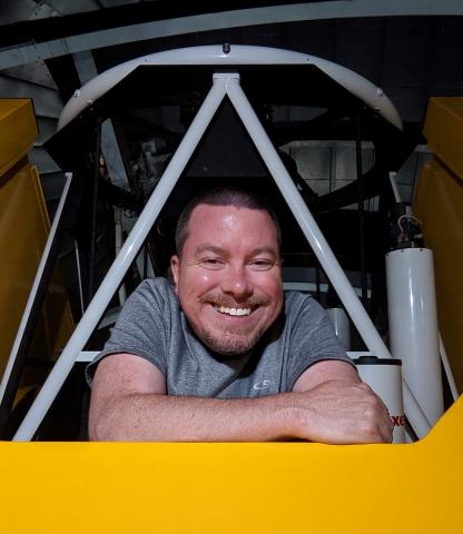 Head shot of Damon smiling and looking out from a telescope structure