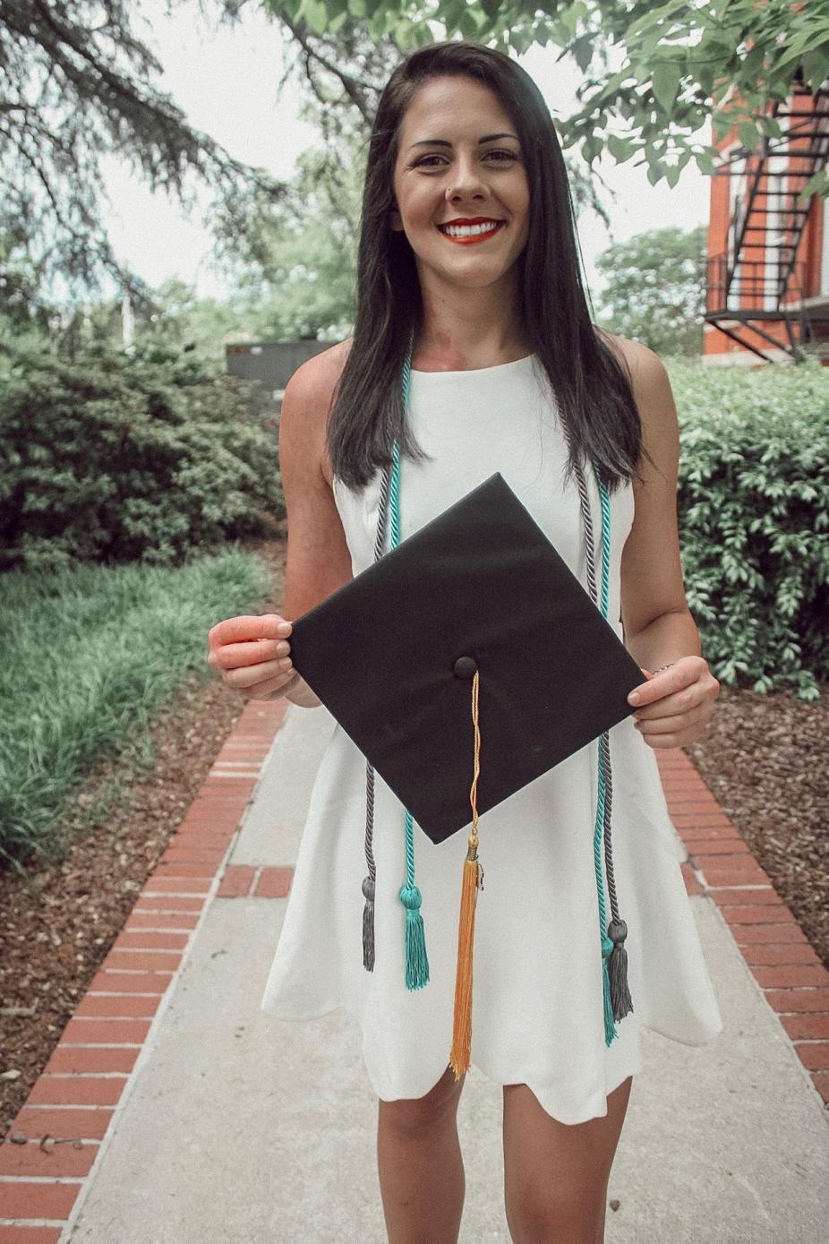 Katherine standing, smiling, and holding a graduation cap.