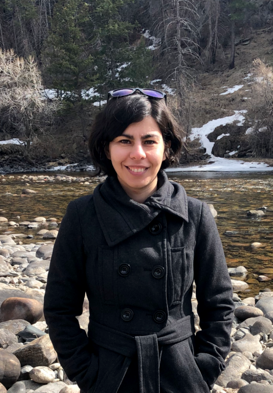 Soudeh Kamali in a winter belted coat standing in front of a rocky stream