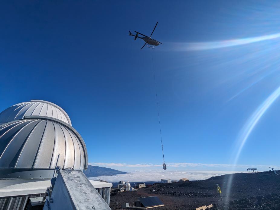 Helicopter flying in batteries and solar panels to MLSO located at 11,200 feet on Mauna Loa. The observatory domes are visible at left.