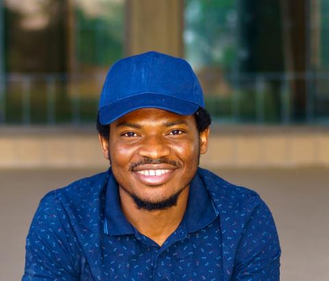 Amadi wearing a bright blue cap and smiling
