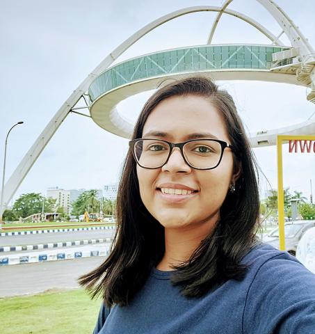 Reveena smiling outdoors in front of a structural steel double arch