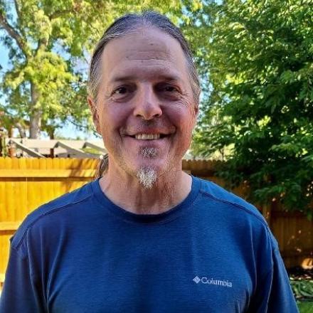 Pat wearing a bright blue t-shirt, standing outdoors, and smiling