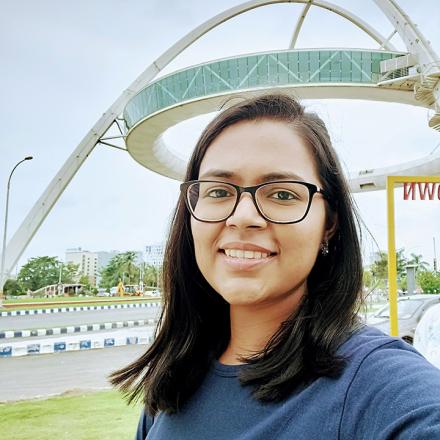 Reveena smiling outdoors in front of a structural steel double arch